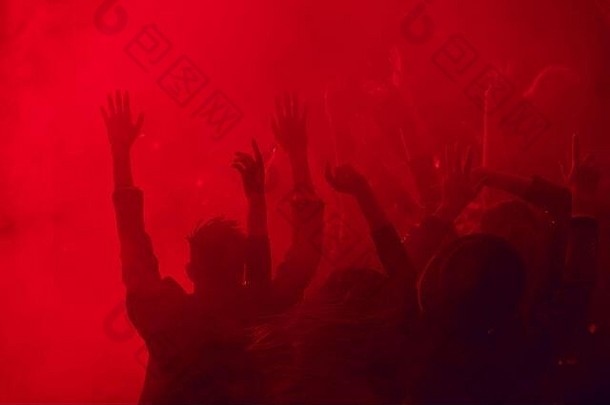 轮廓大集团人跳舞提高手享受聚会，派对烟雾缭绕的夜总会基斯红色的光复制空间