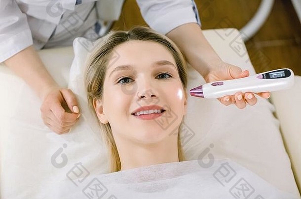 关闭手医生装置激光美容使治疗年轻的微笑金发碧眼的女人删除摩尔疣