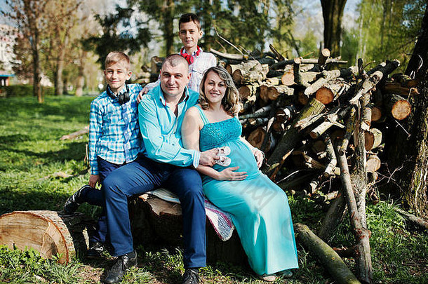 快乐怀孕了家庭儿子穿着绿松石衣服坐着树桩公园