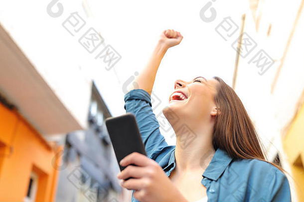 兴奋女人持有聪明的电话庆祝成功街