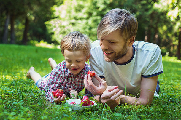 年轻的父亲儿子吃草莓公园野餐户外肖像