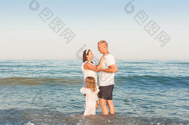 年轻的父母女儿站水海滩拥抱