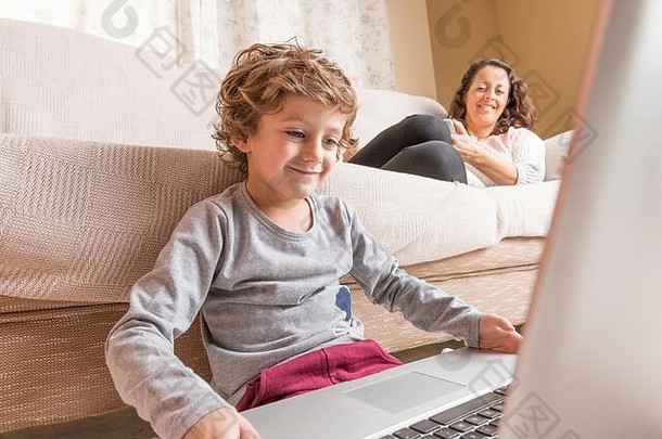 孩子女人坐着沙发看移动PC聪明的电话技术概念家庭