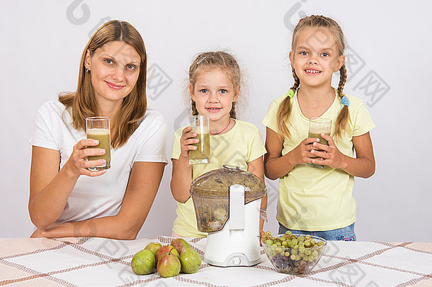 年轻的美丽的妈妈。女儿坐着表格挤压汁梨葡萄榨汁机