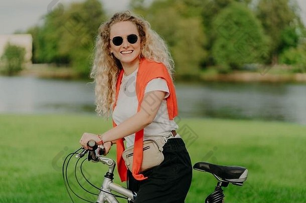 漂亮的女自行车骑手停止美丽的河穿太阳镜白色衬衫跳投肩膀提出了户外运输表达