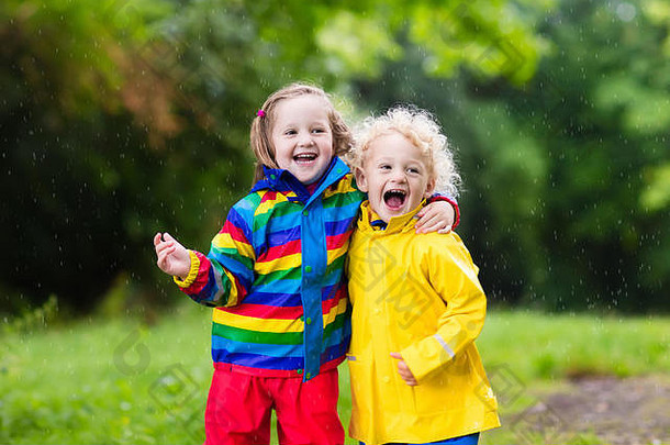男孩女孩玩多雨的夏天公园孩子们色彩斑斓的彩虹夹克防水靴子跳水坑泥雨孩子们细胞膜