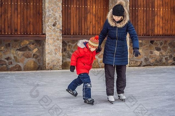 年轻的妈妈。教学儿子冰滑冰户外滑冰溜冰场家庭享受冬天溜冰场在户外