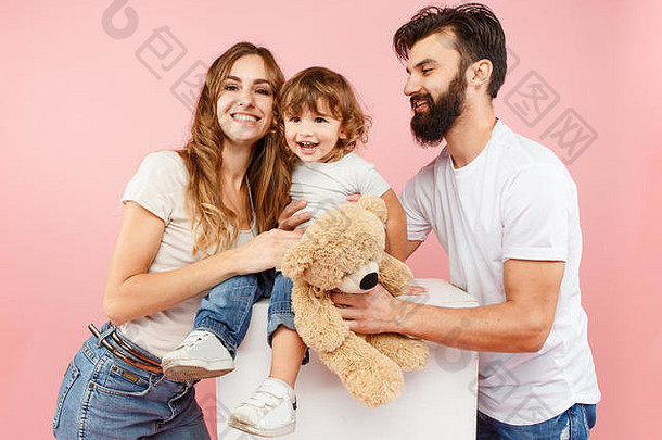 快乐家庭粉红色的工作室背景父亲妈妈。儿子摆姿势泰迪熊玩具