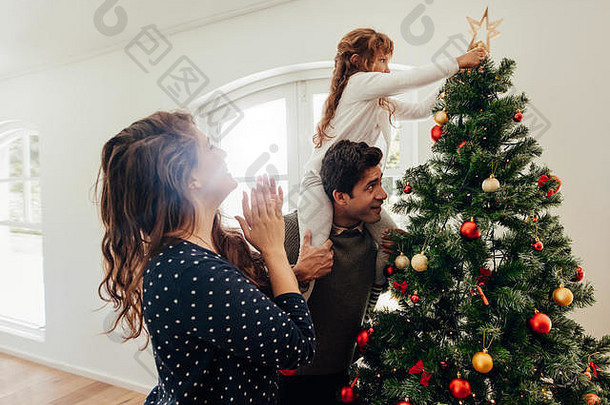 家庭装修圣诞节树年轻的男人。女儿肩膀帮助的地方明星圣诞节树