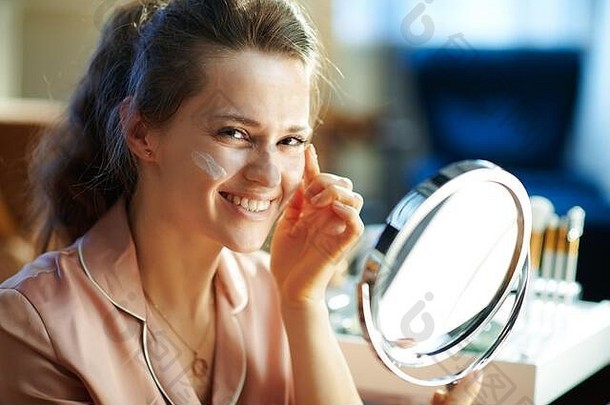 快乐优雅的年女人睡衣镜子应用面部奶油现代生活房间阳光明媚的冬天一天