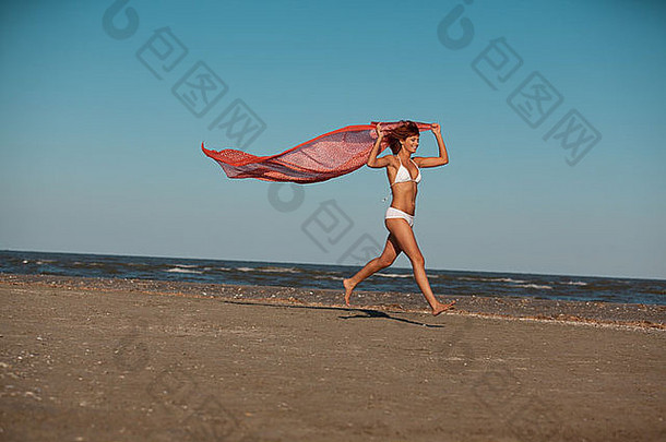 快乐年轻的女人运行海滩持有丝绸围巾手