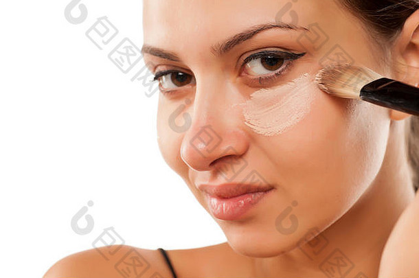 年轻的女人应用液体遮瑕膏眼睛刷