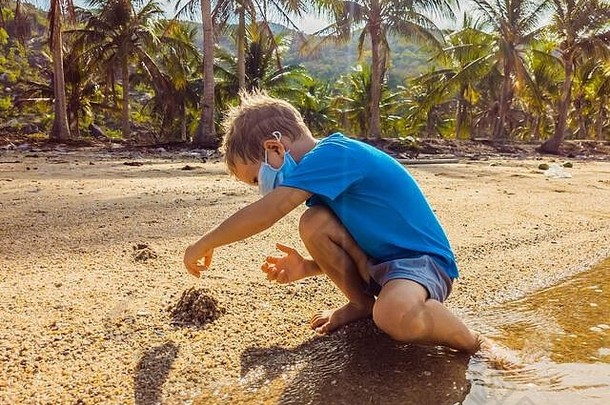 可爱的年轻的金发碧眼的男孩医疗脸面具海滩玩沙子保护空气污染病毒感染正常的
