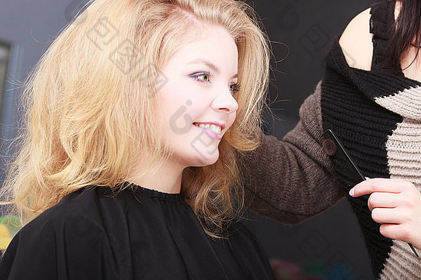 美丽的微笑女孩金发碧眼的波浪头发理发师发型师梳理女客户端年轻的女人美容漂亮的东西或人