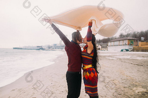 有吸引力的年轻的快乐夫妇接吻白色毯子冬天海滩古董概念