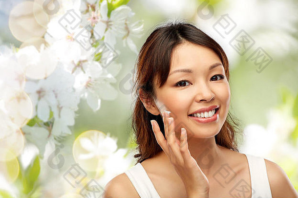 年轻的亚洲女人应用保湿霜脸