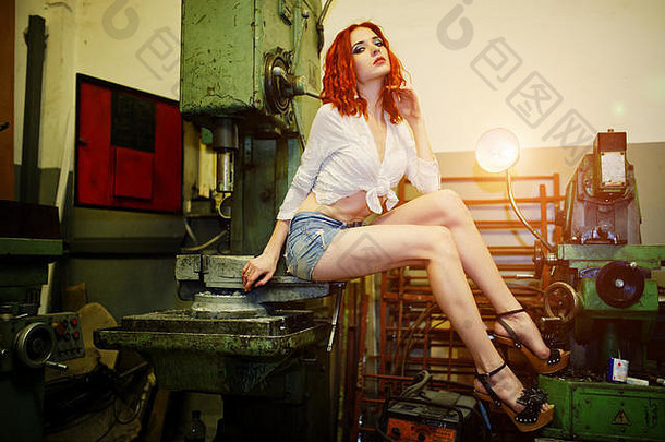红色的头发的女孩穿短牛仔布短裤白色上衣构成工业机工厂