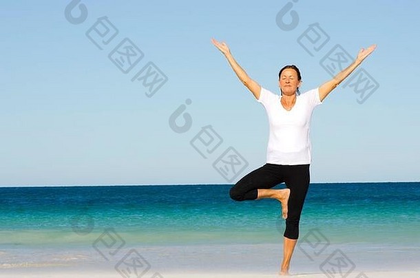 有吸引力的活跃的高级女人保持适合健康的伸展运动普拉提练习海滩海洋蓝色的天空背景复制
