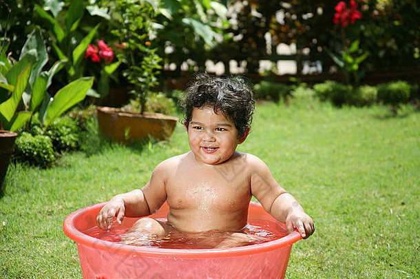 一半一年婴儿坐着红色的塑料浴缸水玩微笑