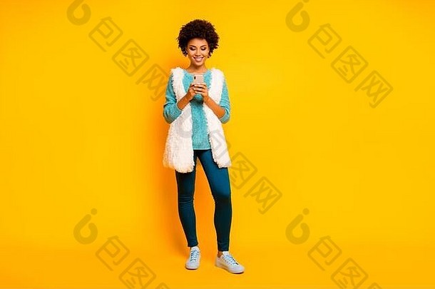 完整的长度照片积极的非洲式发型美国女孩手机读社会媒体新闻聊天穿白色蒂尔毛衣发光蓝色的裤子时尚的时尚的