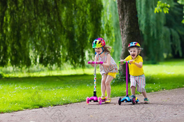 孩子们学习骑踏板车公园阳光明媚的夏天一天学龄前儿童男孩女孩安全头盔骑辊