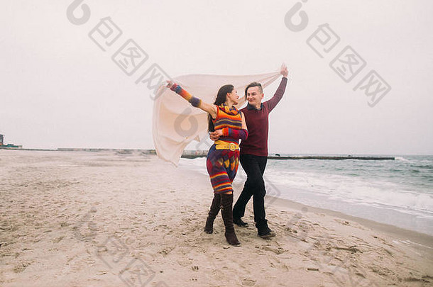 有吸引力的年轻的快乐夫妇包装白色毯子走冬天海滩古董概念