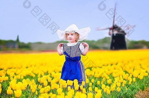 蹒跚学步的女孩穿荷兰传统的国家服装衣服他玩场盛开的郁金香风车