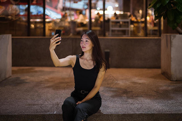 美丽的亚洲女人在户外晚上采取自拍移动电话