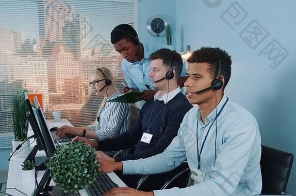 黑色的电话操作符帮助的同事调用中心会说话的客户电话坐着电脑