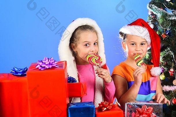 幸福假期概念女孩冬天假期复制空间孩子们圣诞老人老人帽子礼物盒子开放礼物孩子们很高兴脸吃糖果光蓝色的背景