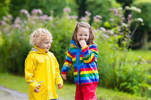 男孩女孩玩多雨的夏天公园孩子们色彩斑斓的彩虹夹克防水靴子跳水坑泥雨孩子们细胞膜
