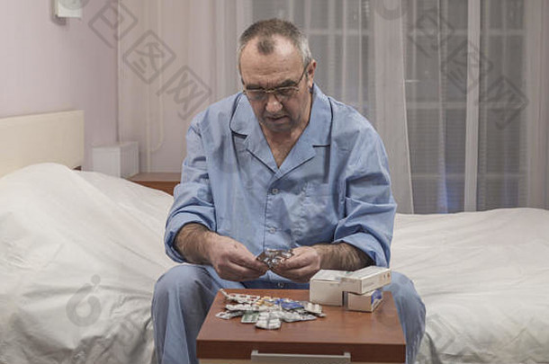 生病的上了年纪的男人。坐在床上选择药物药片