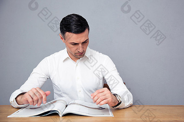 英俊的商人坐着表格阅读杂志灰色的背景
