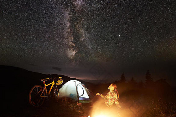 年轻的女人旅游享受晚上野营燃烧篝火照亮旅游帐篷山自行车令人惊异的美丽的晚上天空完整的星星乳白色的天体摄影术