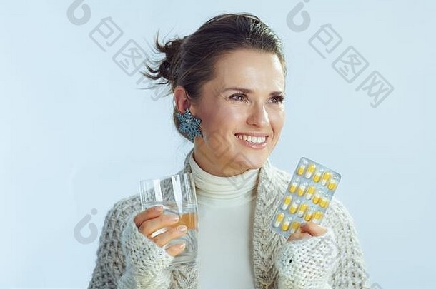 微笑时尚的中间年龄女人卷脖子毛衣开襟羊毛衫玻璃水泡包药片孤立的冬天光蓝色的后台支持