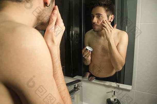 肖像英俊的高加索人少年反射镜子应用保湿霜面部奶油每天护理概念