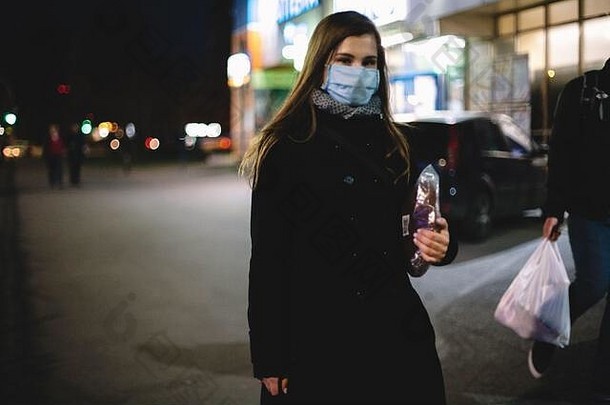 年轻的女人穿脸医疗面具携带面包走城市街晚上