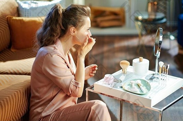 时尚的家庭主妇睡衣应用面部奶油镜子表格化妆品现代房子阳光明媚的冬天一天