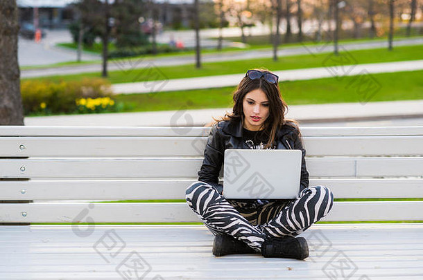 肖像快乐女学生坐着板凳上移动PC在户外相机