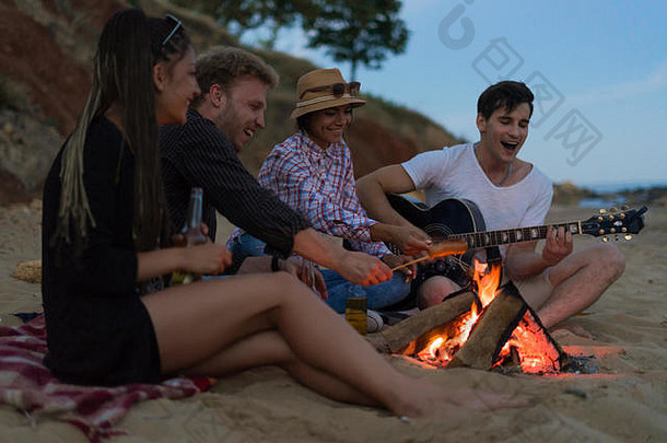 朋友坐着海滩男人。玩吉他
