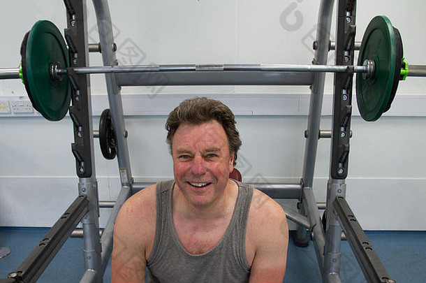 头肩膀肖像男人。微笑相机坐在前面权重健身房锻炼