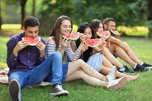 美丽的年轻的人吃多汁的成熟的西瓜在户外快乐朋友坐着草咬一块水果快乐健康的