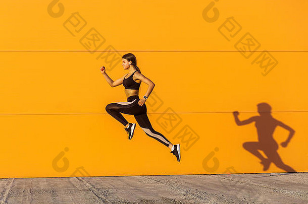 年轻的满意运动美丽的女人适合身体跳运行快点橙色<strong>墙</strong>背景体操运动员跳高露出牙齿的