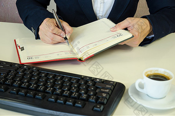 女手写作笔记事本工作桌子上键盘咖啡