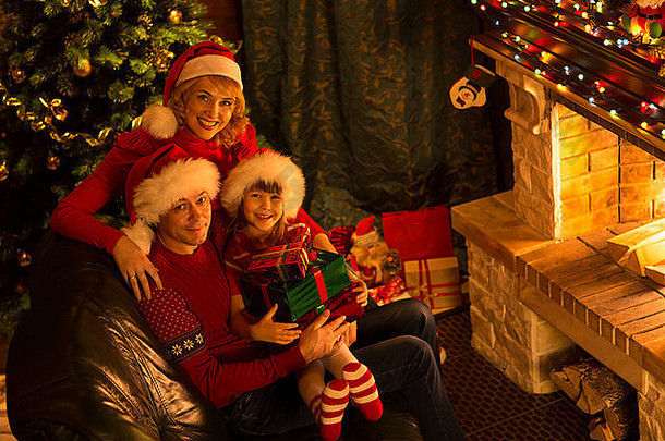 快乐家庭人红色的帽子礼物坐着圣诞节树壁炉
