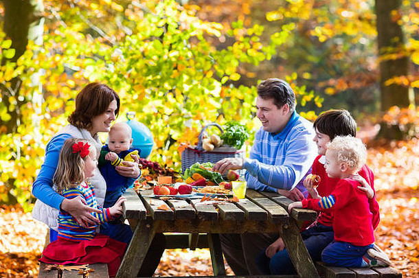 快乐年轻的家庭孩子们烧烤肉使三明治沙拉野餐表格阳光明媚的秋天公园