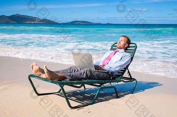 在一个空荡荡的热带海滩上，一位商人坐在沙滩椅上，用笔记本电脑工作
