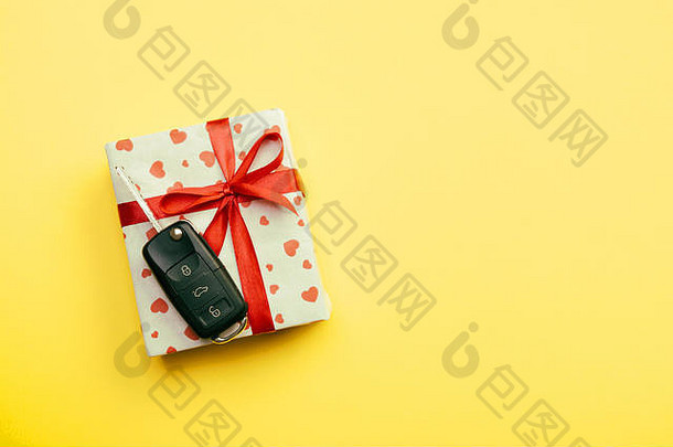 赠送礼品车钥匙概念顶视图。礼品盒上有红色丝带蝴蝶结、心形和黄色背景上的车钥匙。