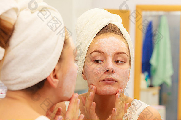 女人在脸上涂面膜保湿护<strong>肤</strong>霜，对着浴室镜子看。呵护<strong>肤</strong>色的女孩分层膏