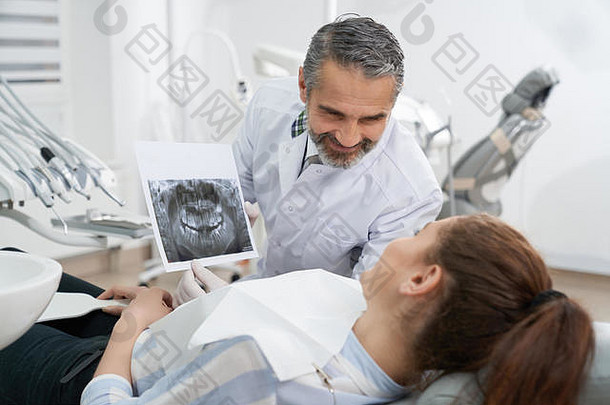 口腔医生向患者展示口腔x光片，咨询。年轻女子躺在牙医椅上，看着扫描。牙齿护理和口腔医学<strong>的</strong>概念。